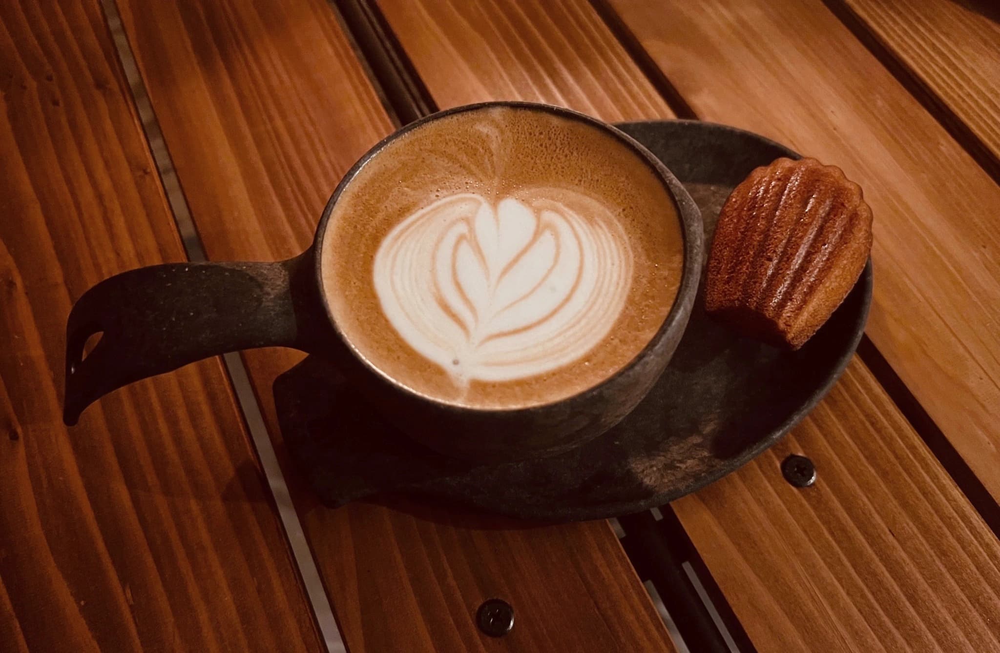 木のテーブルに置かれたカフェラテとマドレーヌ